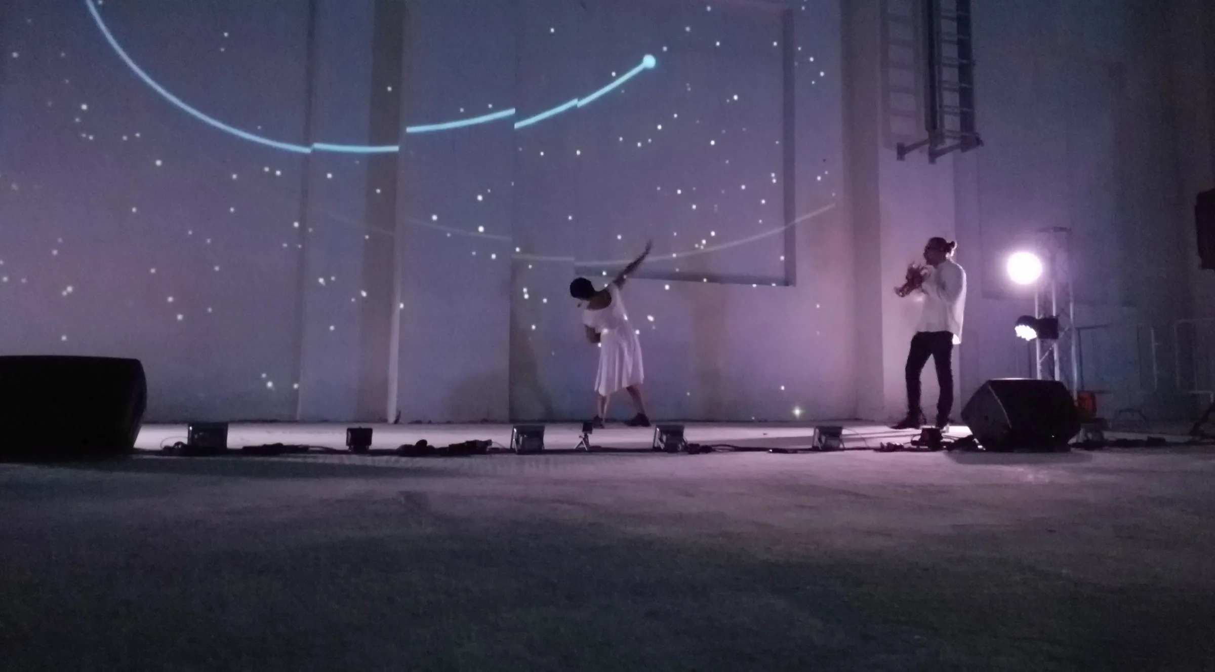 Danza Liquida — danzatrice e trombettista con proiezioni di stelle sulla parete industriale, performance interattiva SUONO E LUCE