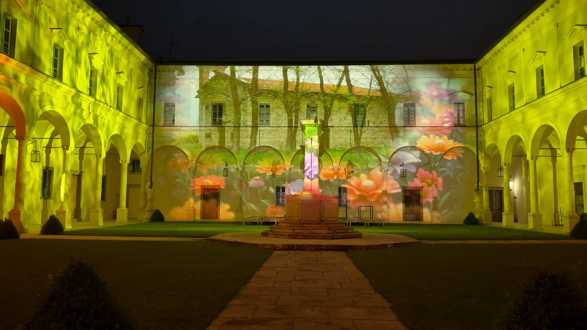 Proiezione di fiori e alberi in verde e giallo sulle pareti del chiostro — videomapping architetturale nell'Abbazia, SUONO E LUCE