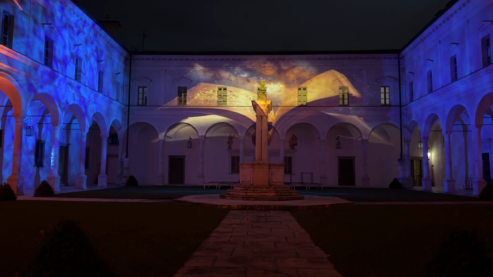 Libro aperto con pagine che girano proiettato sulla facciata del chiostro — il racconto della storia dell'Abbazia inizia, proiezioni architetturali site-specific, SUONO E LUCE